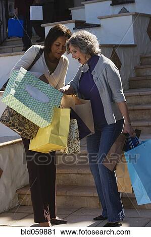 Stock Image - Multi-ethnic women looking in shopping bags. Fotosearch
