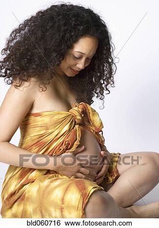 Stock Photograph - Pregnant Mixed Race woman looking at belly. Fotosearch