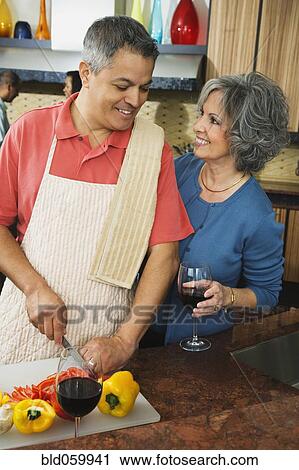 Stock Image - Woman smiling at husband chopping vegetables. Fotosearch