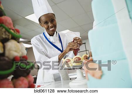Stock Photo - African female pastry chef decorating cake. Fotosearch