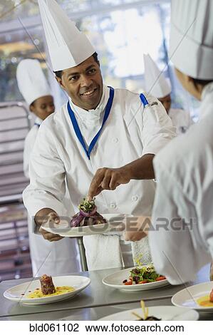 Stock Image - African male chef garnishing plate of food. Fotosearch