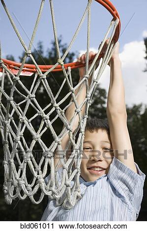 Stock Image - Asian boy hanging from basketball hoop. Fotosearch