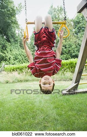 Stock Image - Asian boy hanging upside down on play structure. Fotosearch