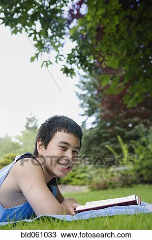 Stock Image - Asian boy reading in grass. Fotosearch