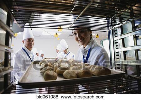 Stock Photo - Asian female baker taking tray of bread off rack. Fotosearch
