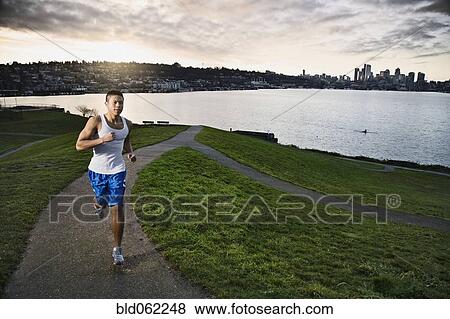 Stock Photo - Asian man jogging along urban waterfront. Fotosearch
