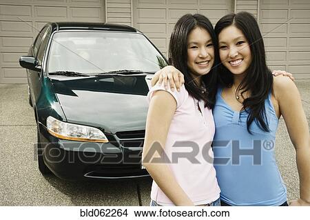 Picture - Asian sisters hugging in driveway. Fotosearch