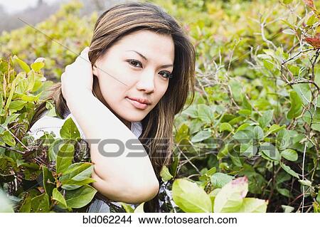Picture - Asian woman standing near bushes. Fotosearch
