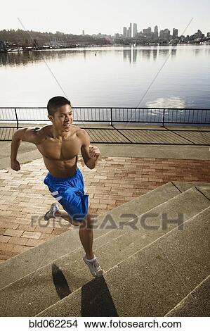 Picture - Bare chested Asian man jogging along urban waterfront. Fotosearch