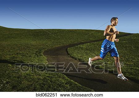 Stock Image - Bare chested Asian man jogging in park. Fotosearch