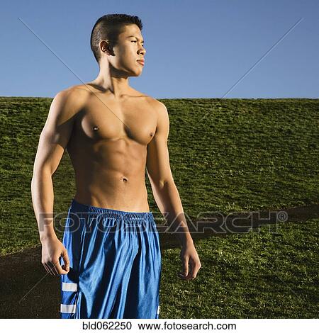 Stock Image - Bare chested Asian man standing in park. Fotosearch