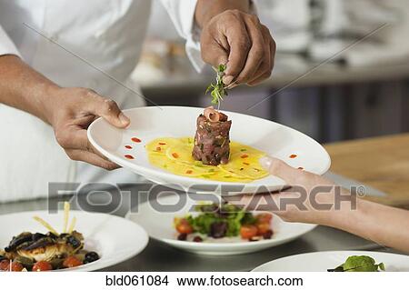 Picture - Chef putting garnish on plate of food. Fotosearch