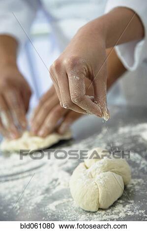 Stock Image - Close up of baker sprinkling flour on dough. Fotosearch