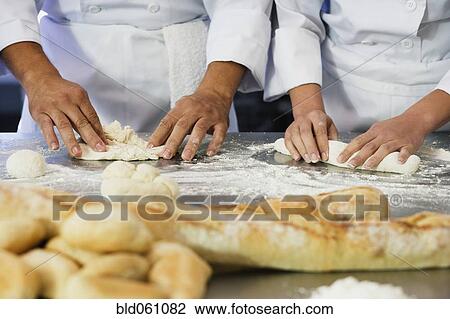 Stock Image - Close up of bakers rolling dough. Fotosearch