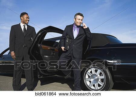 Picture - Hispanic businessman getting out of limousine. Fotosearch