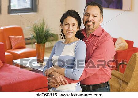 Stock Photography - Hispanic couple hugging in livingroom. Fotosearch