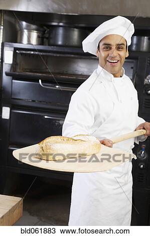 Stock Image - Hispanic male baker holding fresh bread. Fotosearch