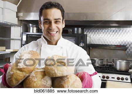 Stock Photography - Hispanic male baker holding fresh bread. Fotosearch