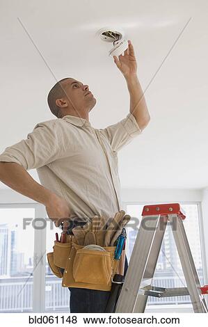 Stock Photo - Hispanic male electrician fixing looking at wiring. Fotosearch