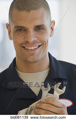 Stock Photo - Hispanic male mechanic holding wrenches. Fotosearch