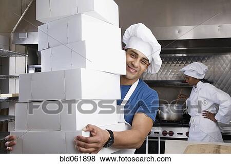 Stock Photo - Hispanic male pastry chef carrying stack of boxes. Fotosearch