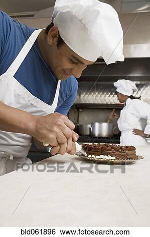 Stock Photograph - Hispanic male pastry chef decorating cake. Fotosearch