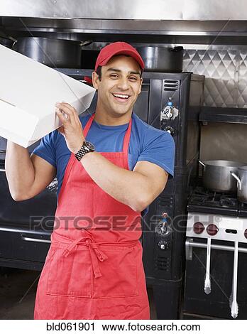 Stock Image - Hispanic male pizza maker holding box. Fotosearch