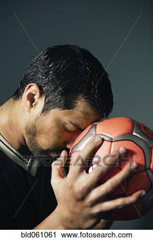 Stock Image - Hispanic male soccer player holding ball against head. Fotosearch