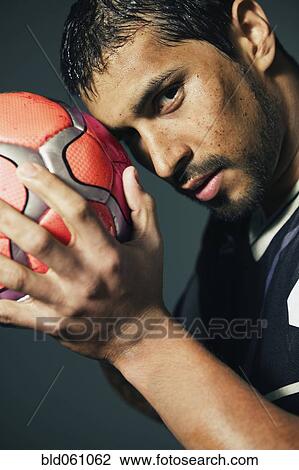 Stock Image - Hispanic male soccer player holding ball against head. Fotosearch
