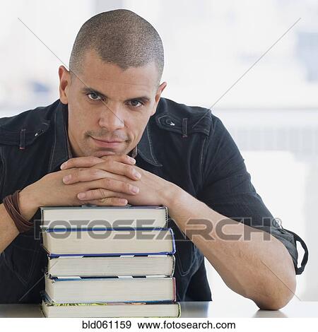 Stock Photo - Hispanic man resting chin on stack of books. Fotosearch