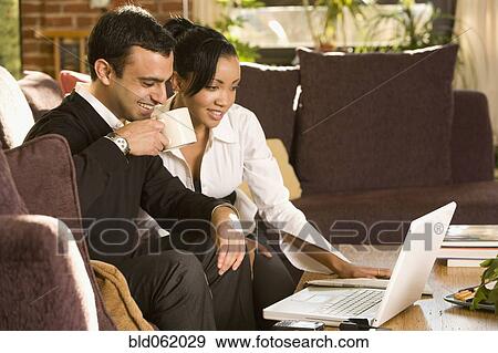 Stock Photo - Mixed race couple working on laptop in living room. Fotosearch