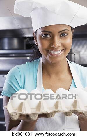 Stock Image - Mixed Race female chef holding eggs. Fotosearch