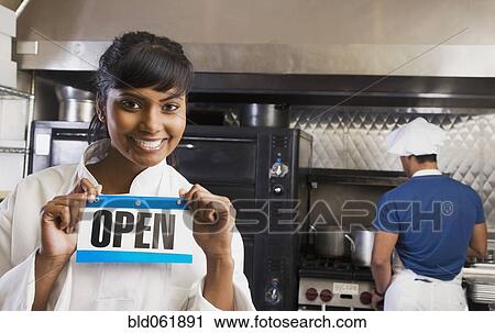 Mixed Race female chef holding Open sign in kitchen View Large Photo Image Stock Image - Mixed Race female chef holding Open sign in kitchen. Fotosearch