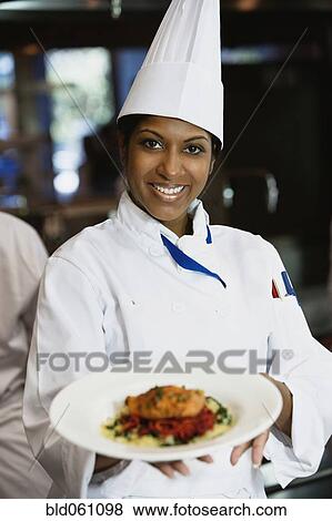 Stock Photo - Mixed Race female chef holding plate of food. Fotosearch