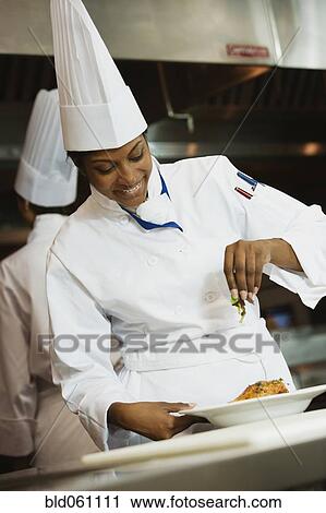 Stock Image - Mixed Race female garnishing plates of food. Fotosearch