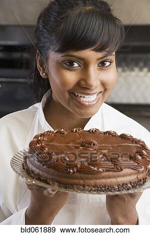 Stock Photo - Mixed Race female pastry chef holding cake. Fotosearch