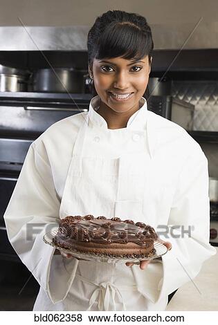 Stock Photo - Mixed Race female pastry chef holding cake. Fotosearch