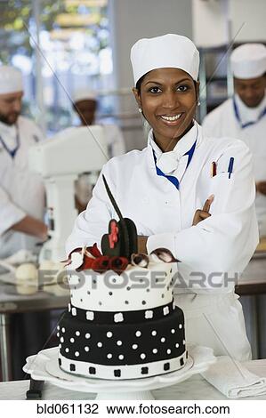 Stock Image - Mixed Race female pastry chef next to cake. Fotosearch