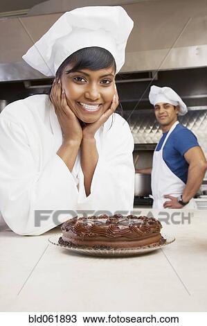 Stock Image - Mixed Race female pastry chef with cake. Fotosearch
