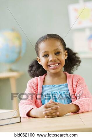 Stock Image - Mixed race girl at desk in classroom. Fotosearch