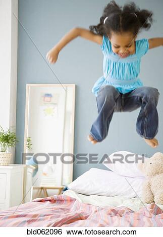 Stock Photograph - Mixed race girl jumping on bed. Fotosearch