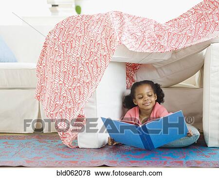 Stock Photo - Mixed race girl reading in living room fort. Fotosearch