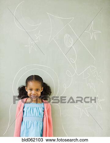 Stock Image - Mixed race girl standing by drawings on blackboard. Fotosearch