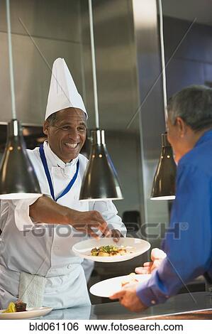 Stock Photograph - Mixed Race male chef garnishing plate of food. Fotosearch