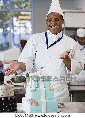 Stock Image - Mixed Race male pastry chef next to cake. Fotosearch