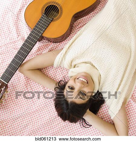 Stock Image - Mixed Race woman laying next to guitar. Fotosearch