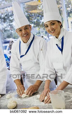 Stock Image - Multi-ethnic bakers rolling dough. Fotosearch