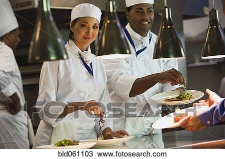 Stock Image - Multi-ethnic chefs garnishing plates of food. Fotosearch