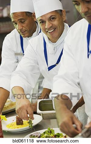 Stock Photo - Multi-ethnic chefs garnishing plates of food. Fotosearch