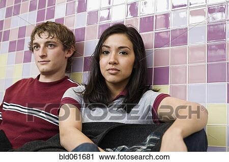 Stock Image - Multi-ethnic couple sitting against wall. Fotosearch